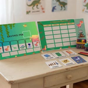 May include: A green dinosaur-themed educational planner set featuring a weekly schedule board with the text PROGRAMMA DIDATTICO and a task board labeled LAVORO PER. Includes small subject cards for Italian, Math, English, History, and Science.