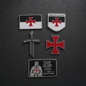 May include: A collection of five metal enamel pins featuring Templar-themed designs. Included are a rectangular flag, a shield with DEUS VULT, a sword with MILITES CHRISTI, a red cross, and a rectangular plaque with a knight and Latin text.