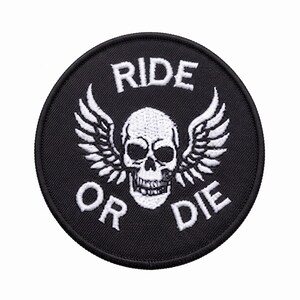 May include: A circular black embroidered patch featuring a white skull with wings in the centre. The text RIDE is stitched in white above the skull, and the text OR DIE is stitched in white below the skull, all enclosed within a black border.