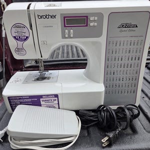 May include: A white Brother Project Runway Limited Edition computerized sewing machine with a digital display, stitch selection chart, and a grey foot pedal with a power cord. The machine features purple accents and labels indicating professional features and a 25-year warranty.