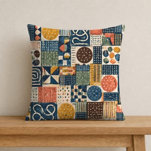 May include: A square throw pillow featuring a patchwork design of various geometric shapes and patterns in shades of navy blue, mustard yellow, terracotta orange, and sage green, with white stitched details throughout the fabric surface.