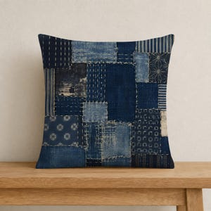 May include: A square throw pillow featuring a patchwork design of various indigo blue fabric swatches. The textile displays a mix of patterns including stripes, geometric shapes, and floral motifs, all joined together with visible white stitching.