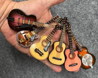 May include: A collection of six miniature guitars in various finishes, including dark red, brown, light wood, and orange. Each small instrument features detailed strings, frets, and bridges, showcasing different body shapes like acoustic and resonator styles.