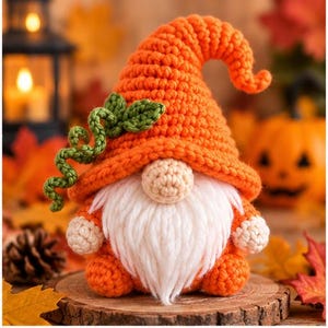 May include: A crochet gnome figurine featuring a tall, textured orange hat adorned with a green crocheted vine. The gnome has a round beige nose, a long white yarn beard, and small beige hands and feet, all crafted in a soft yarn texture.