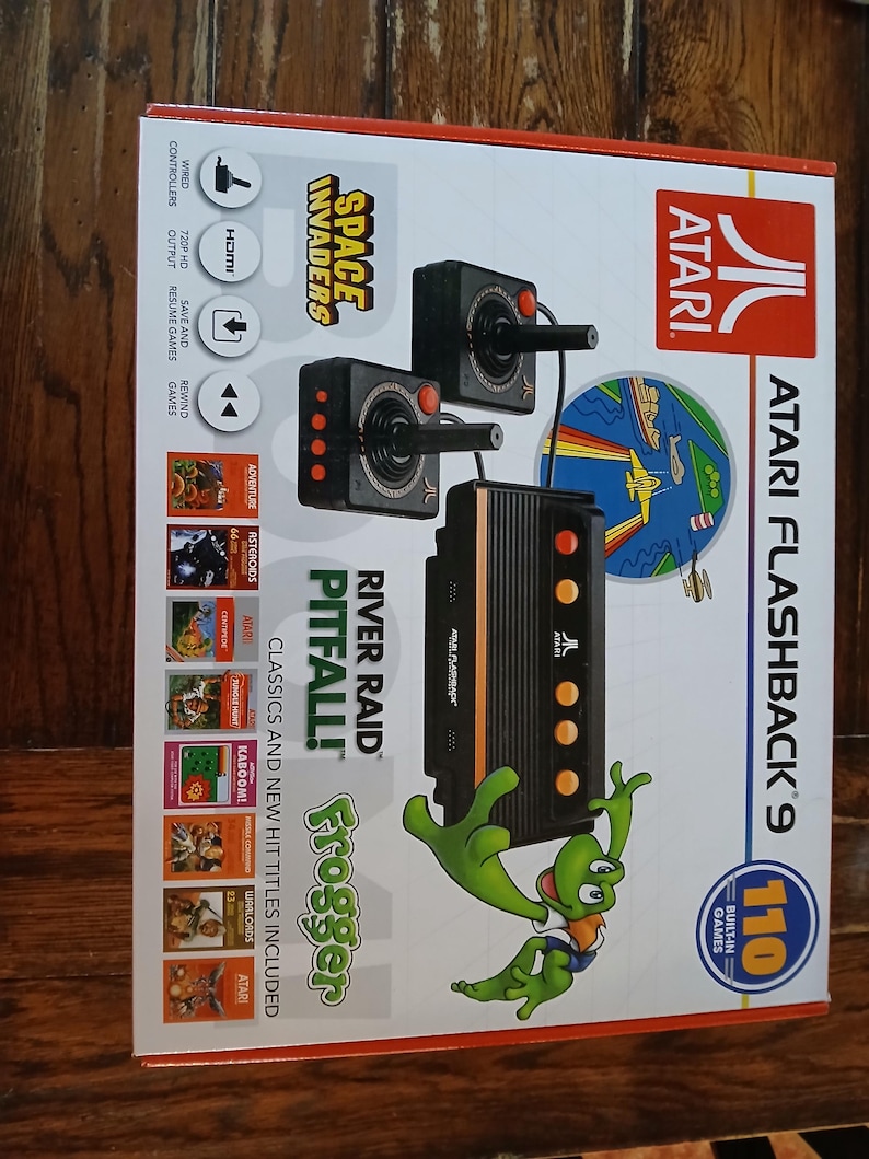 Puede incluir: Caja de consola de juegos Atari Flashback 9 con 110 juegos integrados, dos joysticks con cable y una consola negra. El empaque muestra el logotipo de Atari, t&iacute;tulos como Space Invaders, River Raid, Pitfall, Frogger y salida HDMI.