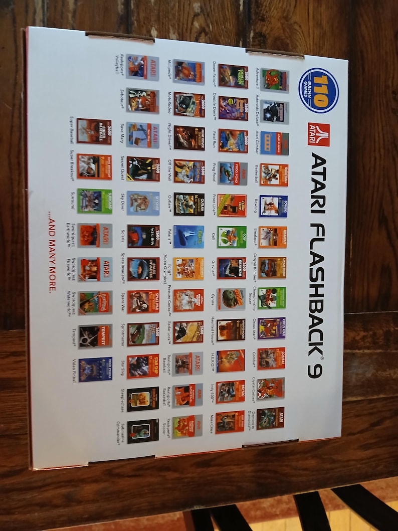 Puede incluir: Una caja blanca de consola de juegos Atari Flashback 9 que presenta una cuadr&iacute;cula de 110 t&iacute;tulos de juegos cl&aacute;sicos, el logotipo de Atari y el texto 110 Built-in Games y ...And Many More. El empaque muestra varias ilustraciones.