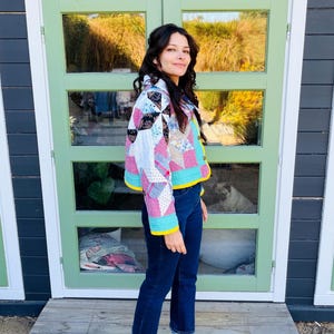 May include: A patchwork jacket with a variety of fabric patterns in pink, blue, and black. The jacket has a yellow trim and is worn with dark blue jeans and green clogs.