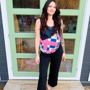 Puede incluir: Una persona con un top sin mangas de mezclilla, pantalones negros y zapatos marrones tejidos. Lleva un bolso acolchado colorido con parches rosas, azules y blancos. El fondo presenta puertas verdes y un porche de madera.