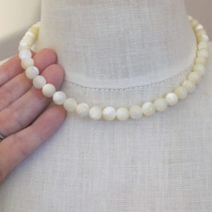 May include: A white mother of pearl bead necklace. The necklace is made of round beads and is approximately 18 inches long.
