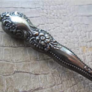 May include: A silver, ornate, decorative handle with a floral design. The handle is smooth and shiny.