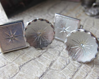 May include: Four silver cufflinks with a starburst design and a clear rhinestone in the center. The cufflinks are on a textured surface.