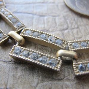 Op de afbeelding: Een gouden kettingarmband met een geometrisch ontwerp. De armband is versierd met heldere strasssteentjes.