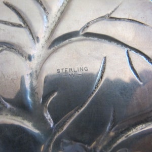 May include: Close-up of a silver tray with a tree design and the words "STERLING -W-  " engraved on the bottom.