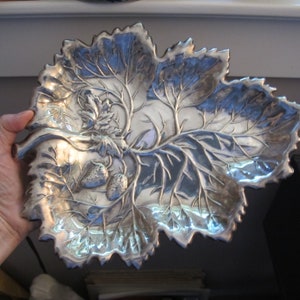 May include: A silver leaf-shaped serving dish with a raised design of leaves and strawberries.