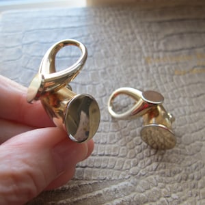 May include: Two gold-toned metal earring closures. The closures are shaped like a loop with a round, flat base.