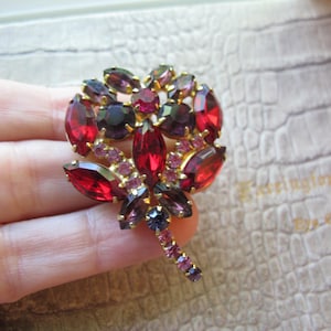 May include: A large, gold-tone brooch with a floral design. The brooch is made of red, pink, and purple rhinestones.