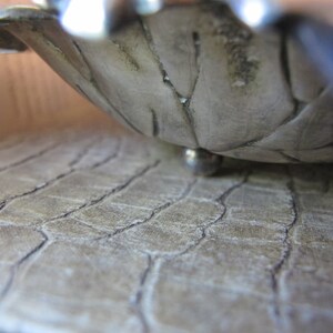 May include: A silver bowl with a textured surface and a round base. The bowl is sitting on a textured surface.