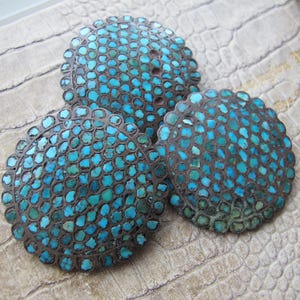 May include: Three round turquoise and silver buttons with a scalloped edge. The buttons are made of small turquoise stones set in silver.