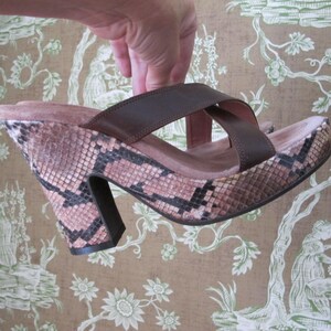 May include: A brown and black snakeskin-patterned platform sandal with a thick heel. The sandal features two brown leather straps across the top and a thick, dark brown heel. The platform is a light pink color.