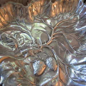 May include: A silver serving dish with a raised design of leaves and strawberries. The dish is made of metal and has a shiny finish.
