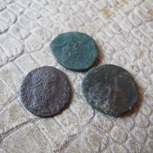 Puede incluir: Tres monedas antiguas de forma circular y aspecto desgastado. Las monedas muestran tonos verdes y marrones, lo que indica su antigüedad. Las superficies muestran signos de desgaste y posibles inscripciones.