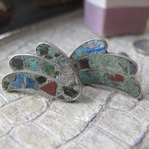 以下が含まれることがあります： カラフルな石のモザイクを特徴とするユニークなデザインのシルバー製のイヤリングのペア。石はシルバーフレームにセットされており、渦巻くパターンを作成しています。