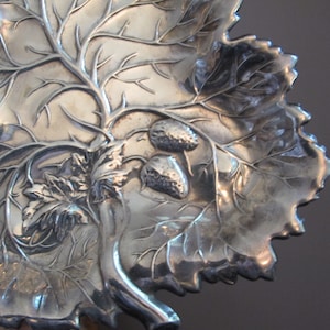 May include: A silver serving dish shaped like a leaf with a vine and strawberries embossed on the surface.