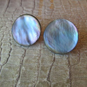 May include: A pair of round, iridescent earrings made from mother of pearl. The earrings have a dark blue, green, and purple color scheme.