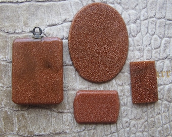 May include: Four pieces of polished, sparkling, reddish-brown gemstone. Shapes include a rectangle with a loop, an oval, a small rectangle, and a rounded rectangle. The gemstones have a glittery, speckled appearance.
