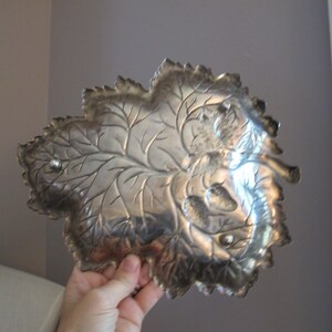May include: Silver leaf-shaped serving tray with a raised design of leaves and acorns. The tray has a slightly tarnished finish.