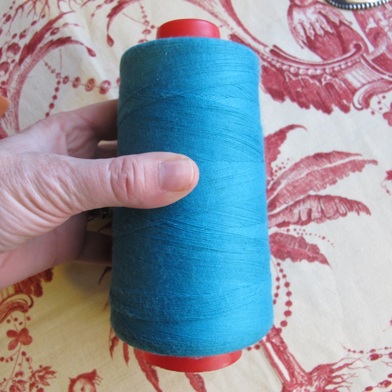 Puede incluir: Una bobina de hilo azul turquesa con extremos de pl&aacute;stico rojo.