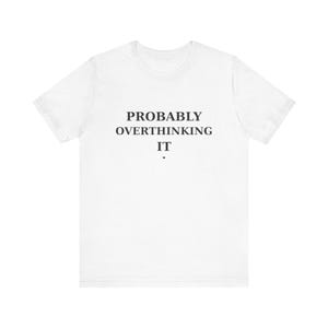May include: A white short-sleeved t-shirt featuring the black text PROBABLY OVERTHINKING IT centered on the chest. Below the text is a small, singular red heart icon. The shirt has a crew neckline and a standard fit, providing a clean look.