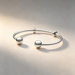 May include: A polished silver-tone open cuff bracelet featuring two large spherical end caps and two smaller cylindrical spacers along the band. The spherical end caps are engraved with the text PANDORA and a small crown symbol.