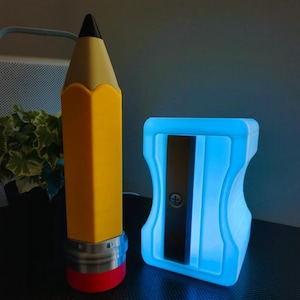 May include: A large yellow pencil-shaped object with a black tip, a silver-colored band, and a red base, positioned next to a glowing light blue pencil sharpener-shaped object featuring a central dark gray blade and a visible screw.
