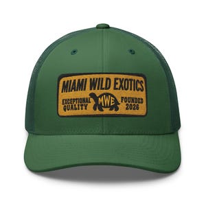 Può includere: Un cappellino trucker verde bosco con una toppa rettangolare su sfondo giallo e testo nero che recita MIAMI WILD EXOTICS, EXCEPTIONAL QUALITY, FOUNDED 2026, e un'icona centrale di tartaruga con le lettere MWE all'interno.