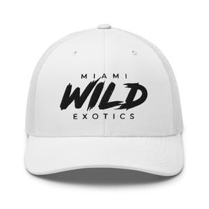 May include: A white trucker cap featuring a mesh back and a solid front panel. The front displays the text MIAMI WILD EXOTICS in black, with the word WILD written in a bold, brush-stroke style font and MIAMI and EXOTICS in a simple sans-serif font.