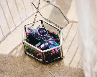 Linda caixinha de alianças geométrica em vidro prateado com cristal de quartzo azul/rosa/roxo sobre um leito de musgo verde e flores de gipsófila rosa.