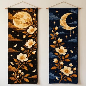 May include: Two rectangular wall hangings featuring cross-stitch patterns. The left piece shows a full moon with white flowers on a black background. The right piece displays a crescent moon and stars with white flowers on a dark blue background.