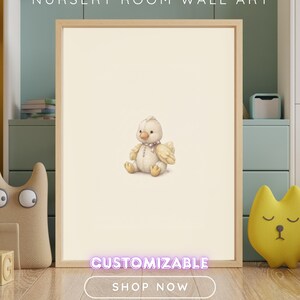 K&ouml;nnte beinhalten: Ein gerahmtes Wandbild mit einer zentralen Illustration eines kleinen, cremefarbenen Pl&uuml;schk&uuml;kens mit einem hellrosa Band um den Hals. Der Text NURSERY ROOM WALL ART, CUSTOMIZABLE und SHOP NOW ist auf dem Bild zu sehen.