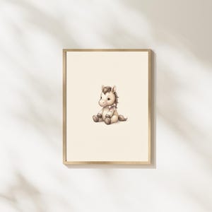 May include: A framed wall art print featuring a light brown cartoon horse sitting down. The horse has a cream-colored muzzle, a dark brown mane and tail, and a small light pink ribbon tied around its neck, all set against a plain off-white background.