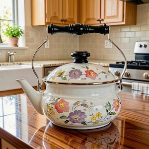 May include: A white enamel tea kettle featuring a colorful floral pattern with pink, purple, and yellow flowers. The kettle has a black handle, a black lid knob, and a metallic rim. The design includes green leaves and stems across the body.