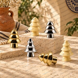 Puede incluir: Una colección de seis pomos decorativos con forma de árbol en varios acabados, incluyendo oro pulido, plata reflectante y crema mate. Cada pomo presenta un diseño cónico escalonado con una base cilíndrica sobre una superficie de piedra.