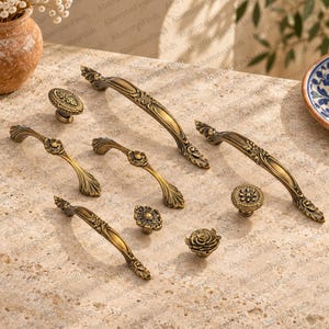 Puede incluir: Una colección de herrajes para armarios de metal en tono latón antiguo, que incluye cuatro tiradores curvos con detalles florales ornamentados y cuatro pomos redondos con patrones en relieve y un diseño de rosa esculpida.