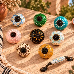 Puede incluir: Una colección de ocho pomos redondos de cerámica y un tirador de cajón de cerámica. Los pomos presentan varios colores, incluyendo azul, verde, turquesa, rosa, negro, blanco, marrón y amarillo, decorados con intrincados patrones pintados.