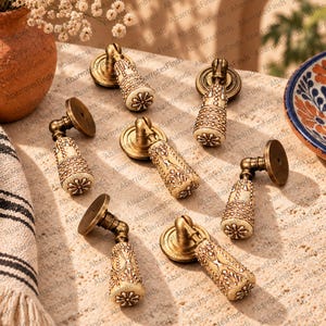 Könnte beinhalten: Ein Set aus sieben hängenden Möbelgriffen mit einer runden Montageplatte aus antikem Messing und einem konischen Keramikgriff. Der Keramikteil ist cremefarben mit braunen Filigranmustern und einem Blumenmotiv an der Unterseite.