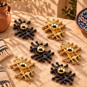 Peut inclure: Un ensemble de six boutons de placard décoratifs disposés en grille. Trois boutons ont une finition noire mate et trois sont en ton doré poli. Chaque bouton présente une sphère centrale entourée d'une structure métallique rayonnante.