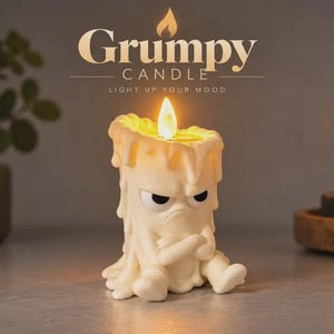 May include: A cream-colored candle shaped like a grumpy character with crossed arms and a furrowed brow. The candle features a lit flame at the top and wax drips down the sides. Above the candle, the text reads Grumpy CANDLE LIGHT UP YOUR MOOD.