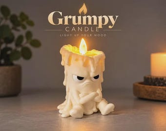 May include: A cream-colored candle shaped like a grumpy character with crossed arms and a furrowed brow. The candle features a lit flame at the top and wax drips down the sides. Above the candle, the text reads Grumpy CANDLE LIGHT UP YOUR MOOD.