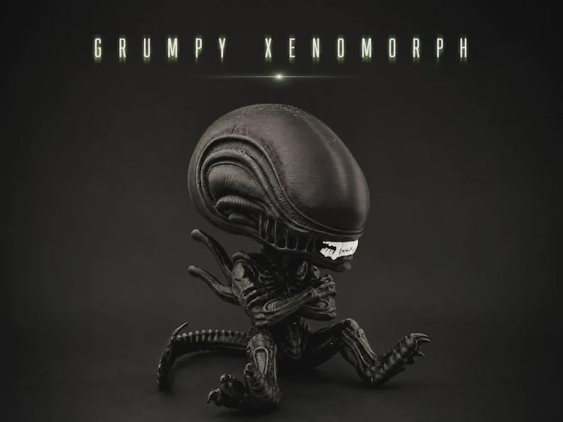 May include: A black Xenomorph figurine with a large, elongated head, white teeth, and arms crossed in a seated position. The text GRUMPY XENOMORPH is displayed in white capital letters above the figure against a dark, solid background.
