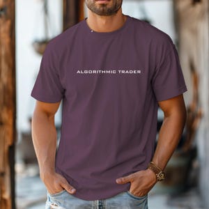 May include: A dark purple short-sleeved t-shirt featuring the text ALGORITHMIC TRADER printed in white capital letters across the center of the chest. The garment has a classic crew neckline and a standard fit, constructed from a solid fabric.
